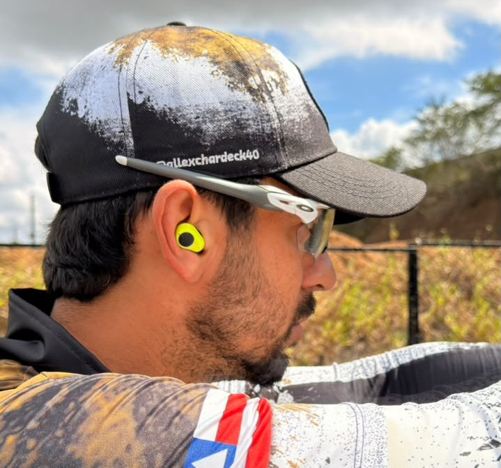 Practical shooter wearing electronic shooting earbuds at an outdoor range